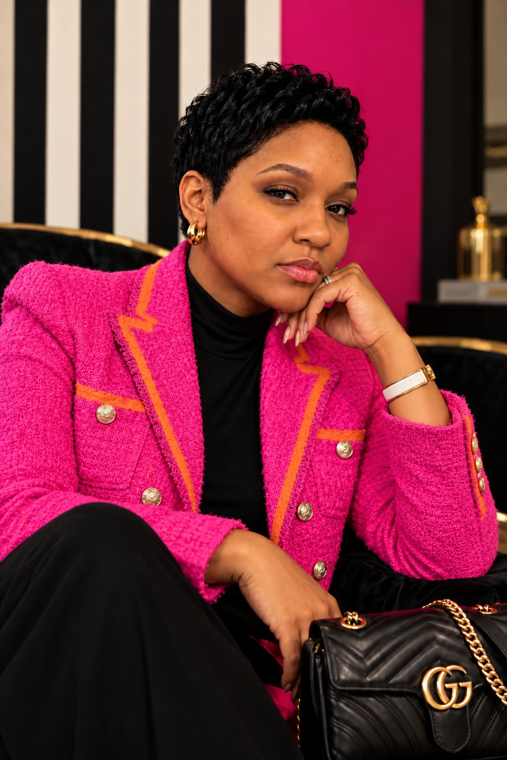Chandice, founder of The Godly Glow Up, in a hot-pink tweed jacket with orange trim, resting her chin on her hand in front of a black-and-ivory striped wall and a hot-pink panel.